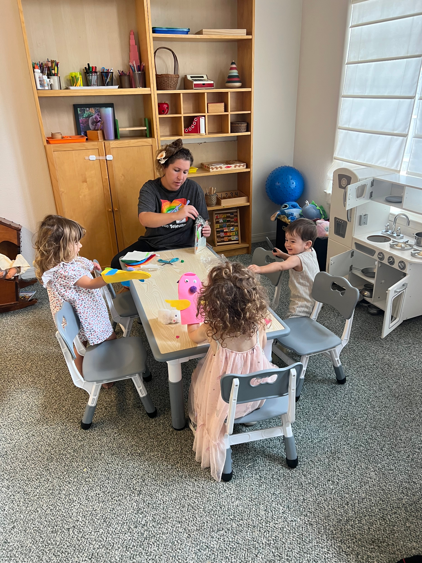 Heidi working on a craft project with three young children at the classroom table